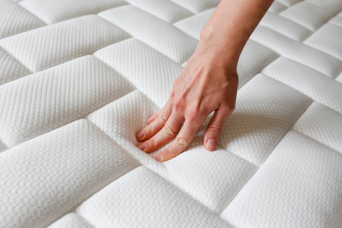 Person pressing hand down into soft mattress.
